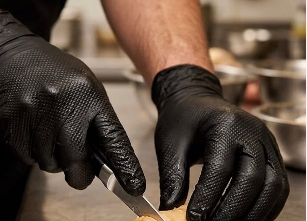 Gloved hands slicing ginger on a stainless kitchen bench